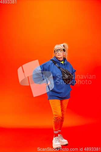 Image of Senior woman in ultra trendy attire isolated on bright orange background