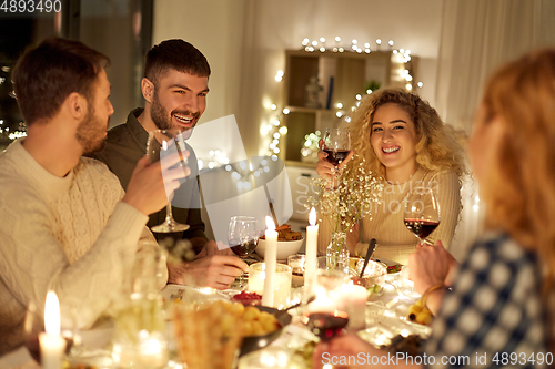 Image of happy friends drinking red wine at christmas party