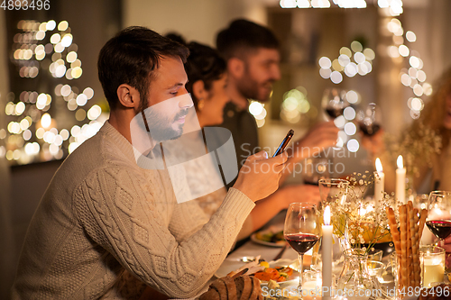 Image of man with smartphone at dinner party with friends