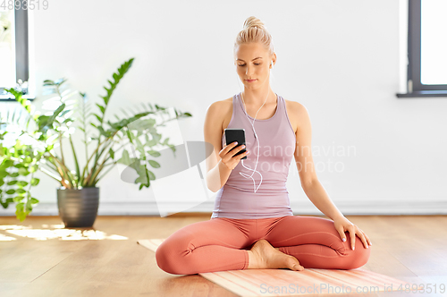 Image of woman with phone and earphones doing yoga at home