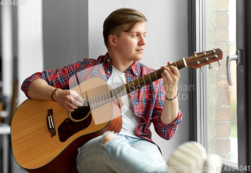 Image of young man playing guitar sitting on windowsill