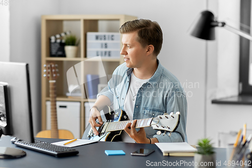 Image of young man with computer playing guitar at home