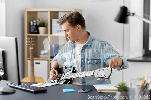 Image of young man with computer playing guitar at home