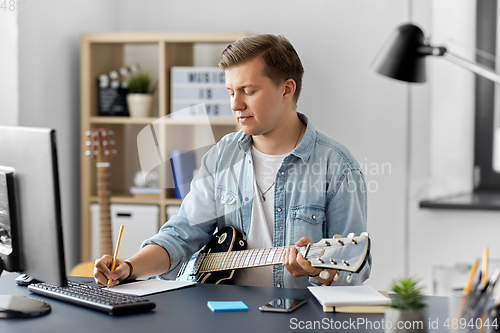 Image of man with guitar writing to music book at home