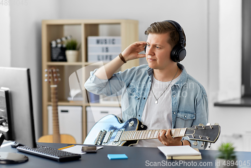 Image of man in headphones playing bass guitar at home