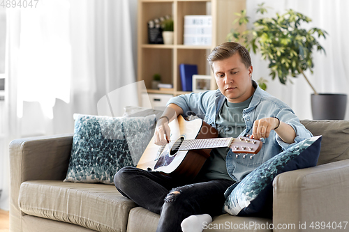 Image of young man playing guitar sitting on sofa at home