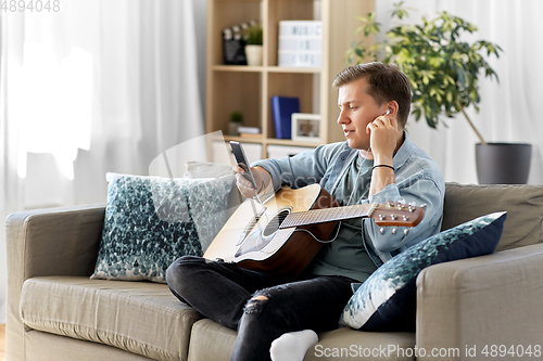 Image of man with guitar, earphones and smartphone at home