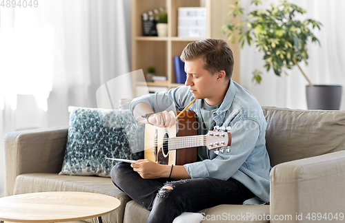 Image of young man with guitar and music book at home