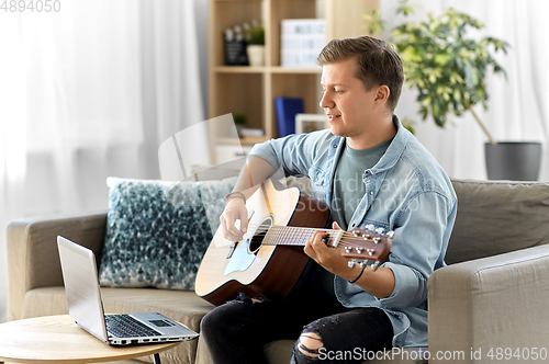 Image of young man with laptop playing guitar at home