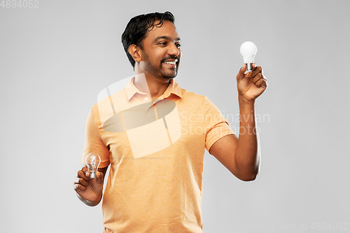 Image of smiling indian man comparing different light bulbs