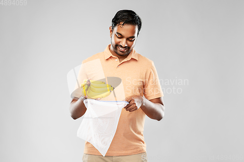 Image of happy man putting bananas into reusable string bag