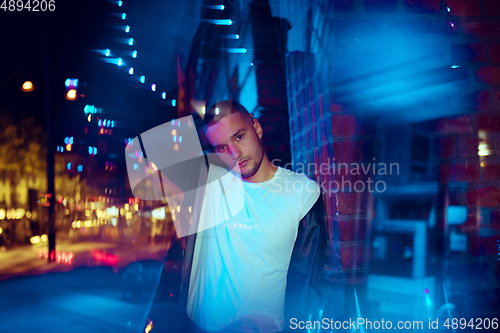 Image of Cinematic portrait of handsome young man in neon lighted room, stylish musician