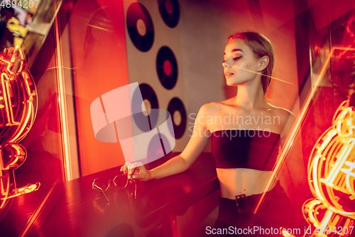 Image of Cinematic portrait of handsome young woman in neon lighted room, stylish musician