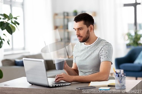 Image of man with laptop drinking coffee at home office