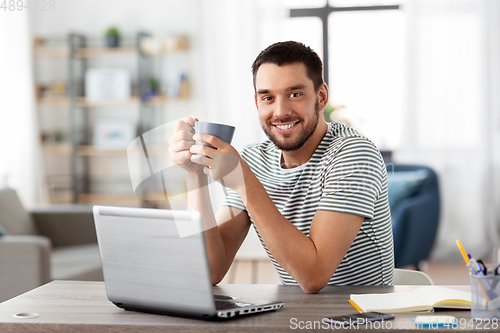 Image of man with laptop drinking coffee at home office