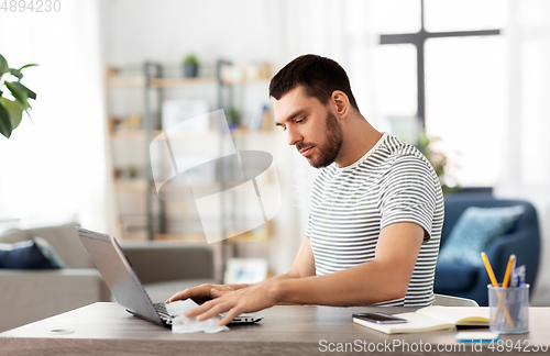 Image of man cleaning laptop with wet wipe at home office