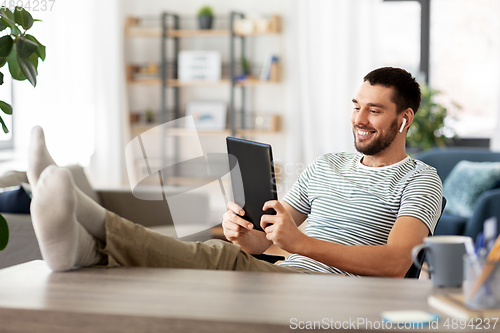 Image of happy man with tablet pc and earphones at home