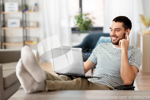 Image of happy man with laptop and earphones at home