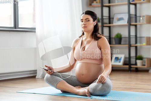 Image of pregnant woman with earphones doing yoga at home