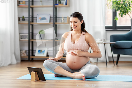 Image of pregnant woman with tablet pc doing sports at home