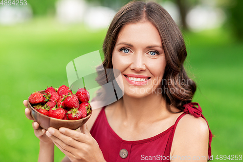 Image of happy woman eating strawberry at summer park