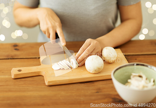 Image of woman cutting champignons by knife on board