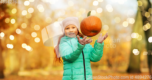 Image of happy girl playing with pumpkin at autumn park