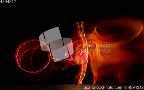 Image of Young flexible female gymnast isolated on black studio background in mixed light,