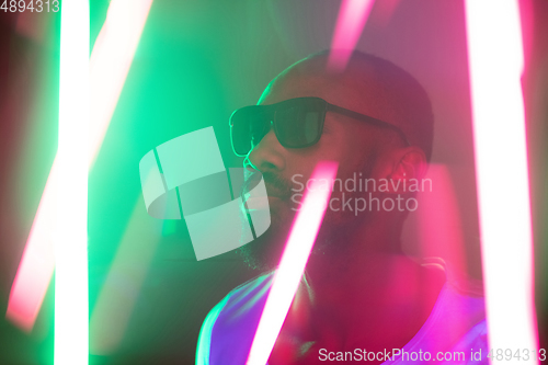 Image of Cinematic portrait of handsome young man in neon lighted room, stylish musician