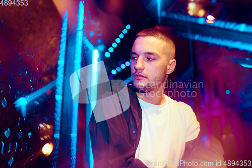 Image of Cinematic portrait of handsome young man in neon lighted room, stylish musician