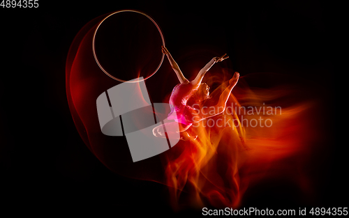 Image of Young flexible female gymnast isolated on black studio background in mixed light,