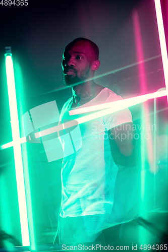 Image of Cinematic portrait of handsome young man in neon lighted room, stylish musician