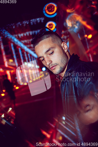 Image of Cinematic portrait of handsome young man in neon lighted room, stylish musician