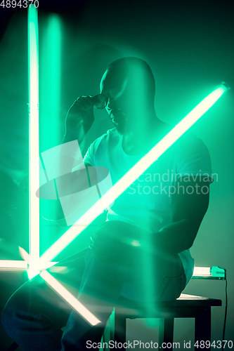 Image of Cinematic portrait of handsome young man in neon lighted room, stylish musician