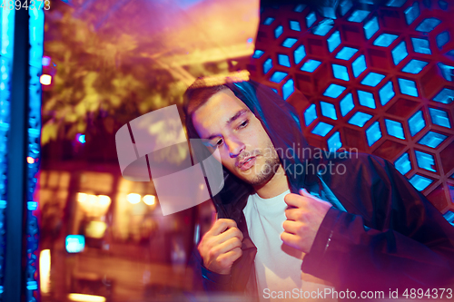 Image of Cinematic portrait of handsome young man in neon lighted room, stylish musician