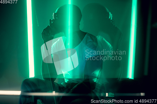 Image of Cinematic portrait of handsome young man in neon lighted room, stylish musician