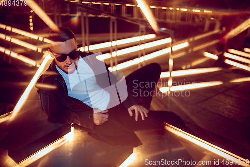 Image of Cinematic portrait of handsome young man in neon lighted room, stylish musician