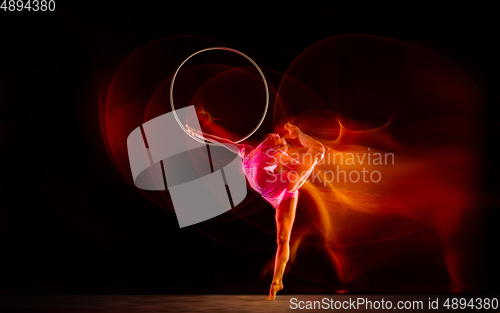 Image of Young flexible female gymnast isolated on black studio background in mixed light,