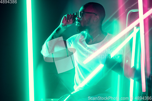 Image of Cinematic portrait of handsome young man in neon lighted room, stylish musician