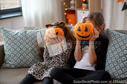 Image of girls in halloween costumes with pumpkins at home
