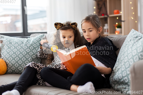 Image of girls in halloween costumes reading book at home