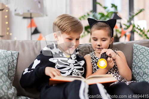 Image of kids in halloween costumes reading book at home