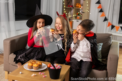 Image of kids in halloween costumes eating cupcakes at home