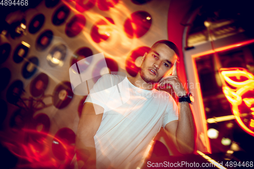 Image of Cinematic portrait of handsome young man in neon lighted room, stylish musician