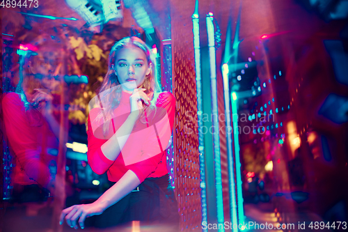 Image of Cinematic portrait of handsome young woman in neon lighted room, stylish musician