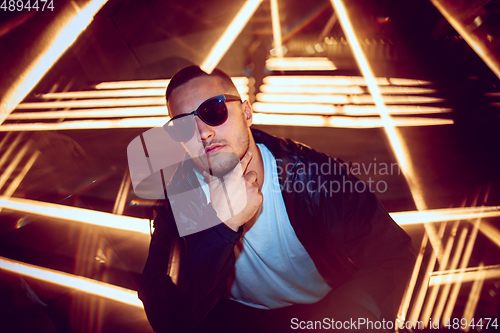 Image of Cinematic portrait of handsome young man in neon lighted room, stylish musician