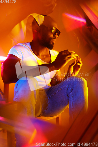 Image of Cinematic portrait of handsome young man in neon lighted room, stylish musician