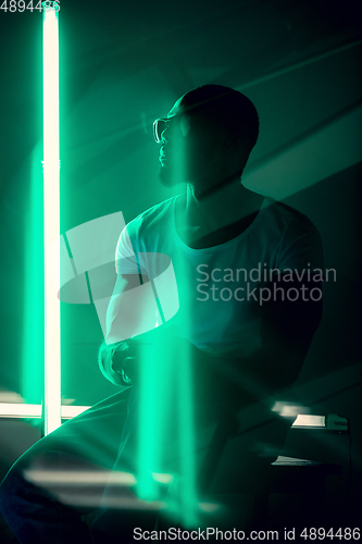 Image of Cinematic portrait of handsome young man in neon lighted room, stylish musician