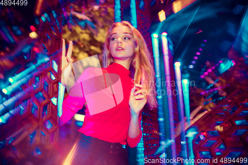 Image of Cinematic portrait of handsome young woman in neon lighted room, stylish musician