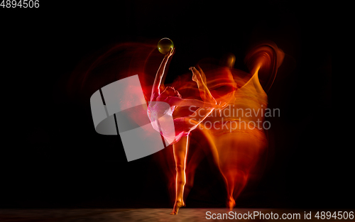 Image of Young flexible female gymnast isolated on black studio background in mixed light,